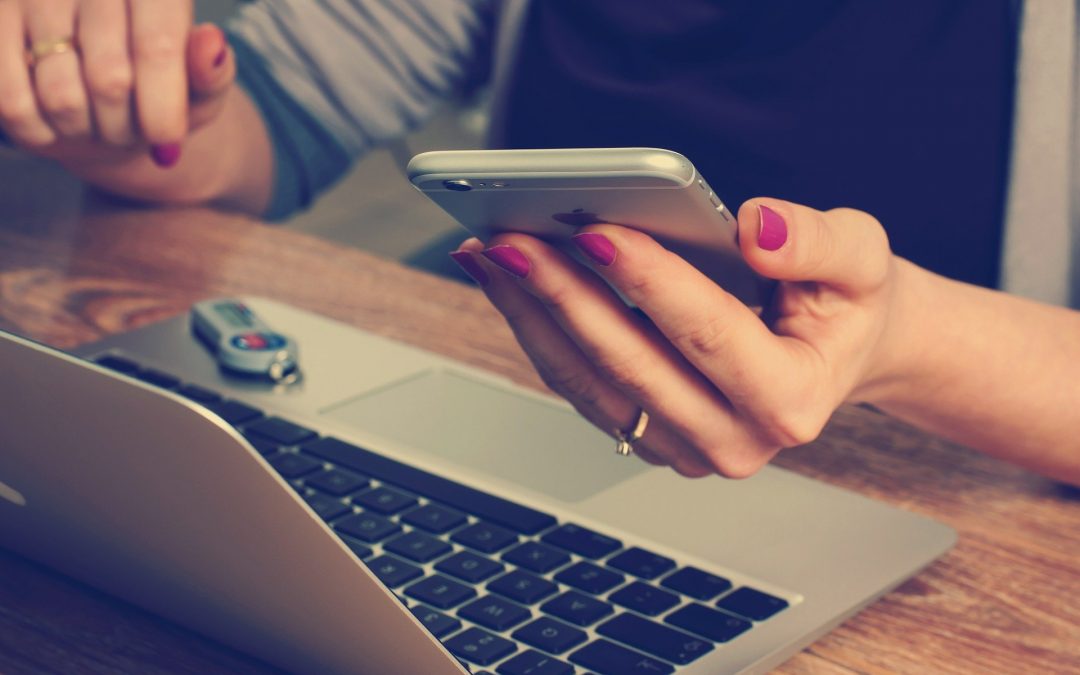 Woman typing on phone in front of laptop