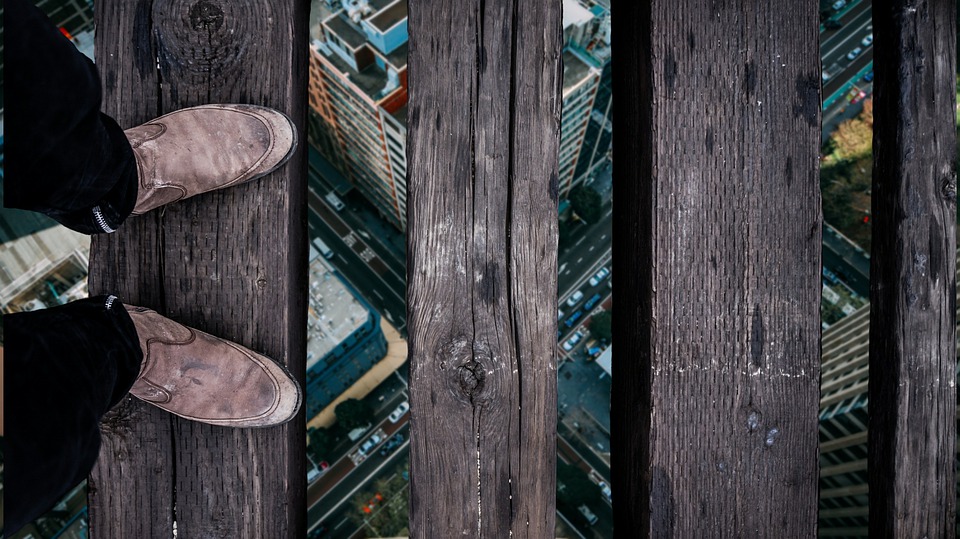 Prerson standing on wooden board suspended high above a city view.